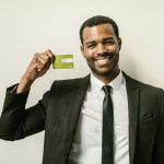 Smiling businessman in a suit displaying a green credit card indoors.
