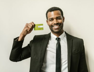 Smiling businessman in a suit displaying a green credit card indoors.