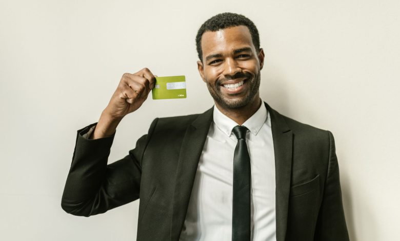 Smiling businessman in a suit displaying a green credit card indoors.