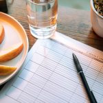Flat lay featuring apple slices, a calorie counter chart, pen, and a glass of water for a healthy lifestyle.