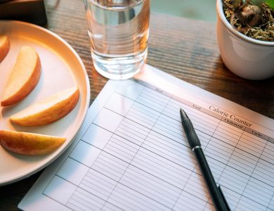 Flat lay featuring apple slices, a calorie counter chart, pen, and a glass of water for a healthy lifestyle.