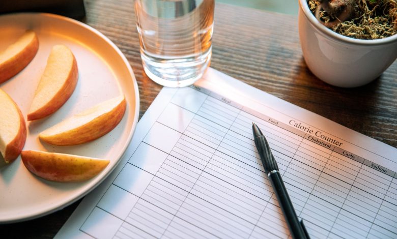 Flat lay featuring apple slices, a calorie counter chart, pen, and a glass of water for a healthy lifestyle.
