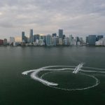 Aerial shot of Miami's skyline with watercraft patterns on the ocean surface.