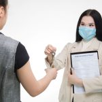 Real estate agent in a face mask hands keys to a client, illustrating safe business practices.