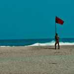 woman in black and white dress holding red flag standing on beach during daytime