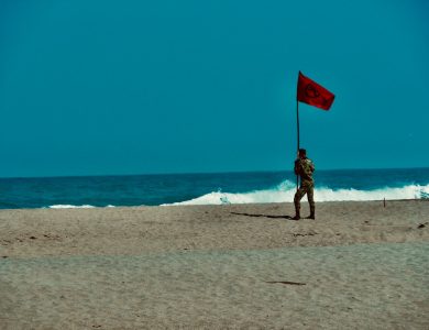 woman in black and white dress holding red flag standing on beach during daytime