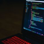 Red backlit keyboard and code on laptop screen create a tech-focused ambiance.