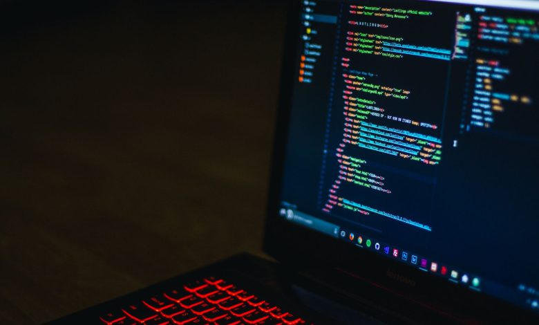 Red backlit keyboard and code on laptop screen create a tech-focused ambiance.