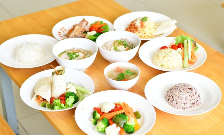 A variety of healthy dishes including rice, soup, and vegetables served on a wooden table.