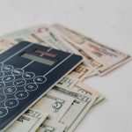 A close-up of a calculator and US dollar banknotes, symbolizing financial calculation and budgeting.