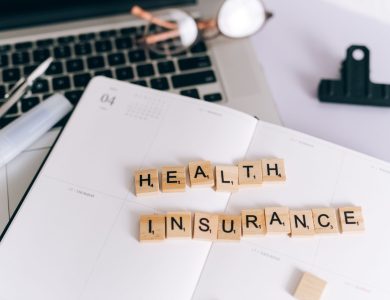 Close-up of Scrabble tiles spelling 'Health Insurance' on a planner with a laptop.