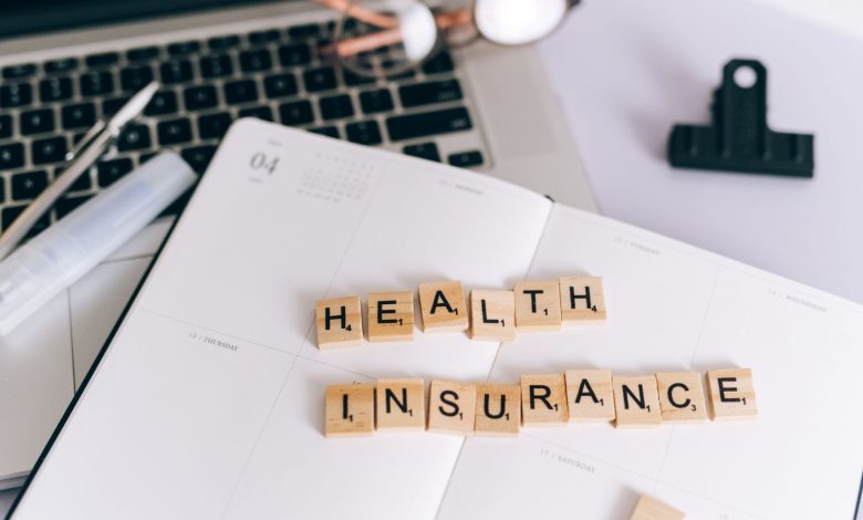 Close-up of Scrabble tiles spelling 'Health Insurance' on a planner with a laptop.