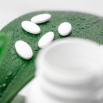 Close-up of white pills on a dew-covered leaf with a blurred bottle foreground.