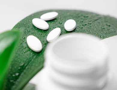 Close-up of white pills on a dew-covered leaf with a blurred bottle foreground.