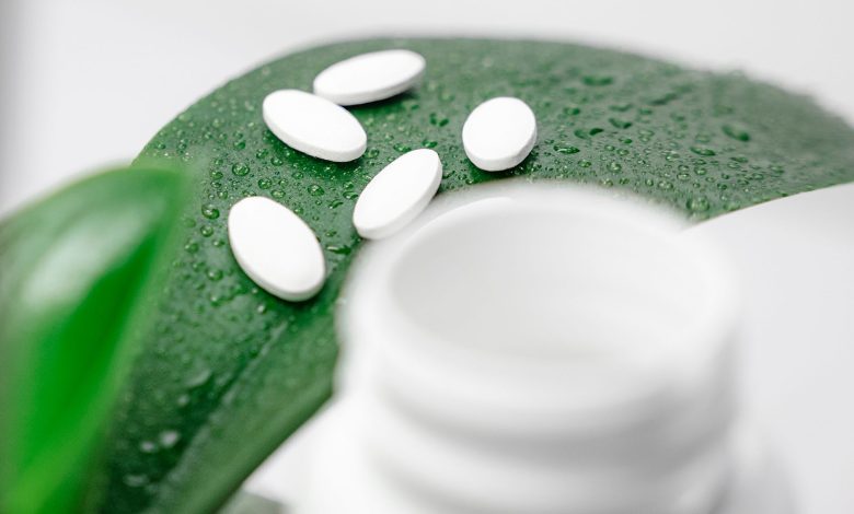 Close-up of white pills on a dew-covered leaf with a blurred bottle foreground.