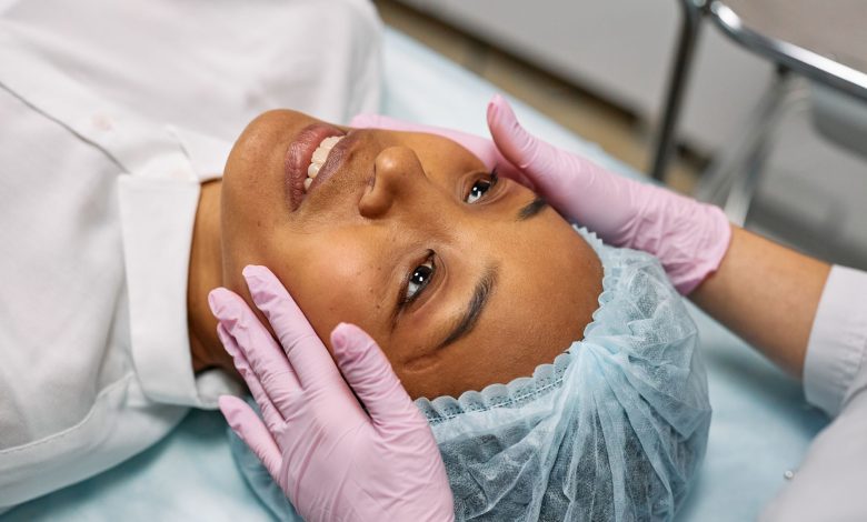 A woman receiving a facial treatment in a spa, wearing a hairnet while hands in gloves gently touch her face.