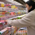 Masked woman shopping for beverages in a supermarket aisle