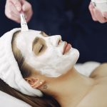 Close-up of a woman with eyes closed enjoying a calming facial mask application at a spa.