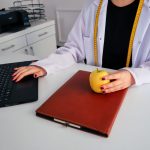 A dietician sitting at a desk with a laptop and apple, symbolizing healthy working lifestyle.