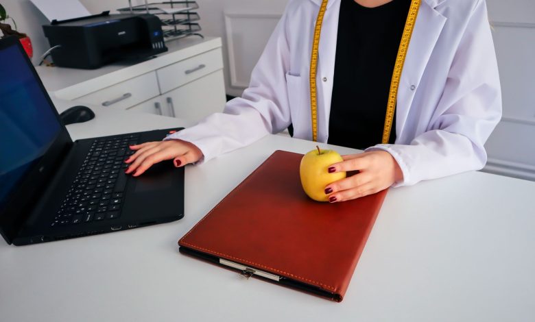 A dietician sitting at a desk with a laptop and apple, symbolizing healthy working lifestyle.