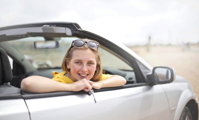 A young woman smiles joyfully while leaning out of a convertible car, enjoying a sunny day.